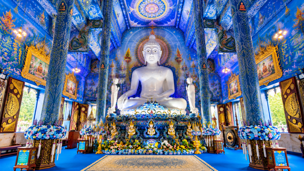 Large white Buddha statue inside the Blue Temple (Wat Rong Suea Ten) in Chiang Rai, Thailand, surrounded by intricate blue and gold decorations.