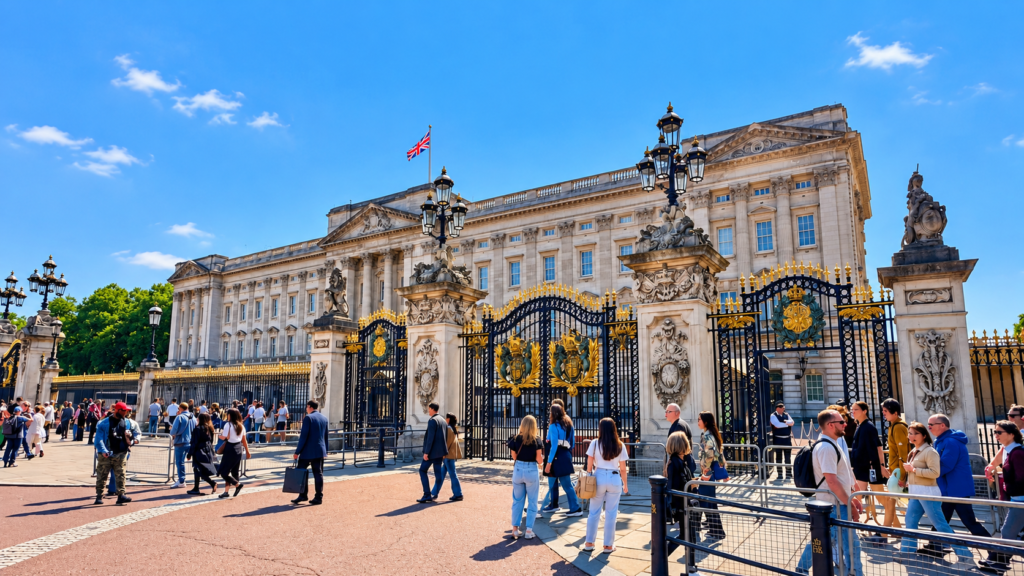 Buckingham Palace in London, featuring its grand royal gates, historic architecture and visitors on a sunny day.