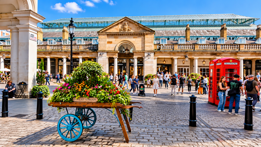 Covent Garden Market in London, featuring colourful flower displays, a red telephone box, historic architecture and visitors exploring the lively piazza.