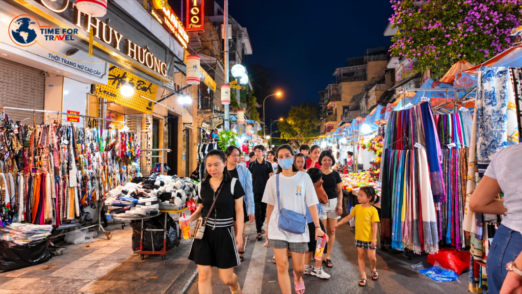 Tourists and locals exploring Hanoi Night Market in Vietnam, surrounded by colourful clothing stalls and street vendors.