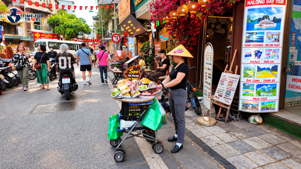 Street vendor wearing a traditional Vietnamese conical hat selling fresh fruit in Hanoi's busy Old Quarter, Vietnam.