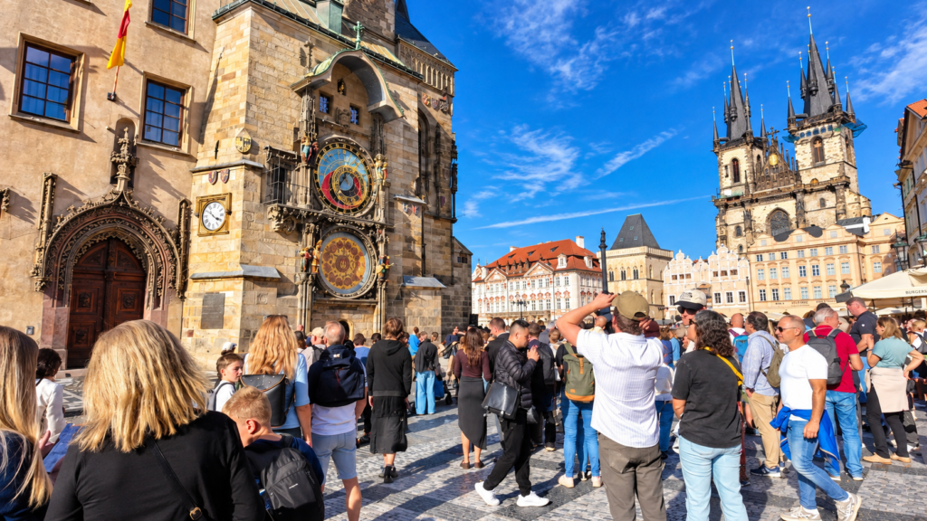 Prague Astronomical Clock on the Old Town Hall, with tourists gathering in Old Town Square and the Church of Our Lady before Týn in the background.