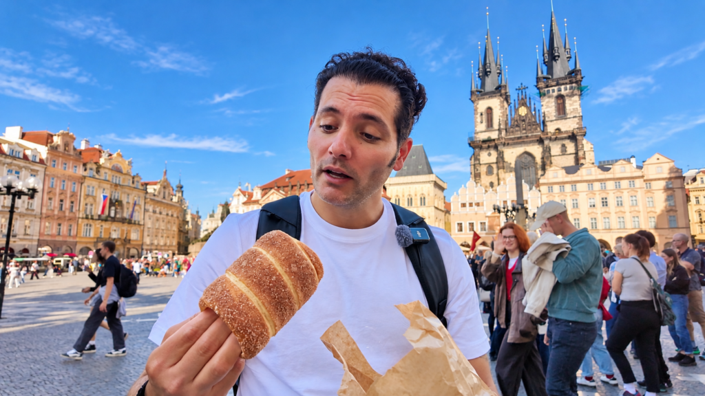 Arash holding a traditional chimney cake (trdelník) in Prague's Old Town Square, with the Church of Our Lady before Týn in the background.