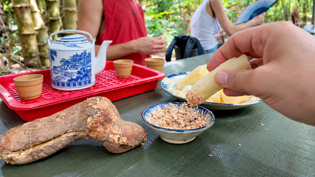 Tasting boiled cassava dipped in crushed peanuts and salt at the Cu Chi Tunnels in Vietnam, served with traditional Vietnamese tea.