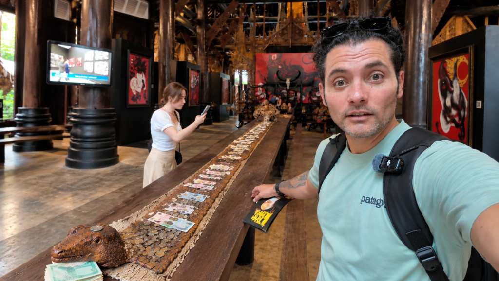 Exploring the Black House Museum in Chiang Rai, Thailand, with a friend photographing a snake display decorated with Thai banknotes and coins.