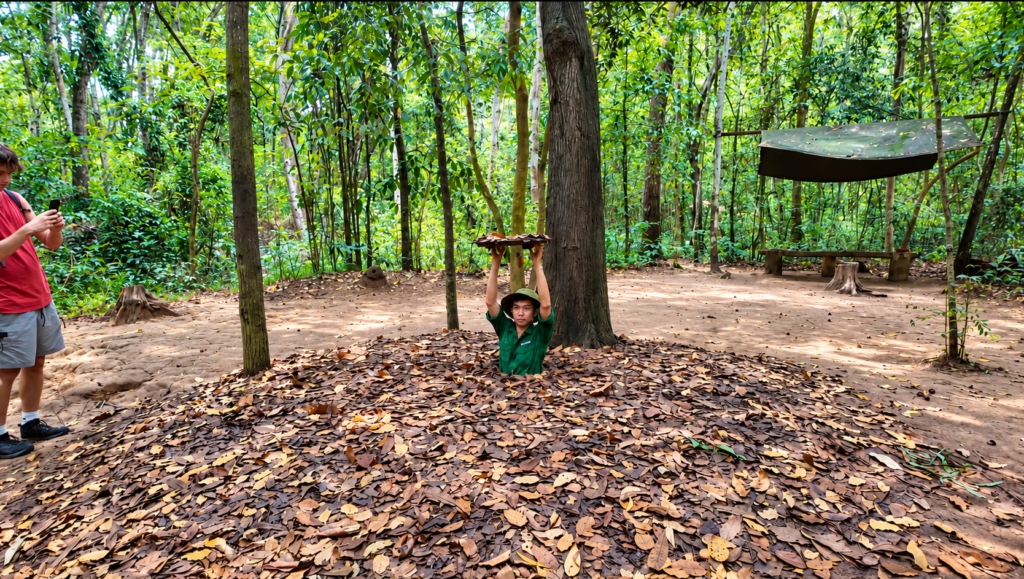 Vietnamese guide demonstrating a hidden tunnel entrance at the Cu Chi Tunnels in Vietnam.
