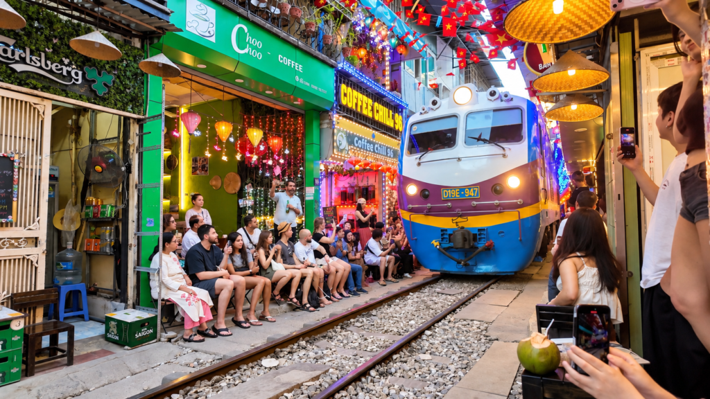 Train passing through Hanoi Train Street in Vietnam, with tourists sitting outside colourful railway cafés
